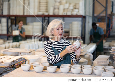 Mature woman ceramist arranging new bowls in workshop Mature woman ceramist arranging new bowls in workshop 110936493