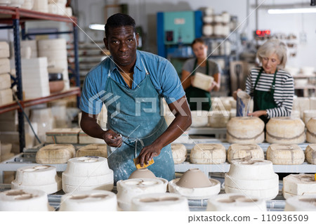 African american man using foam sponge smooths out roughness and irregularities on freshly made pottery 110936509