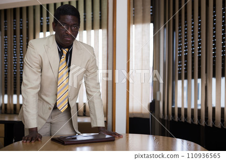 Portrait of a focused african american businessman standing near a desk in a conference room Portrait of a focused african american businessman standing near a desk in a conference room 110936565