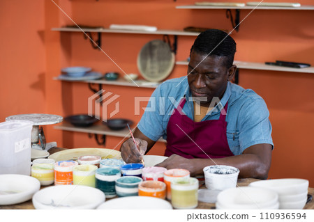 Male craftsman painting clay plates acrylic paints in art studio 110936594