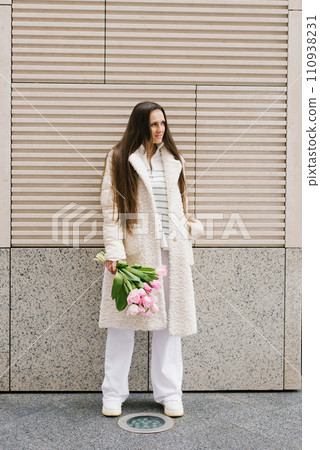 Young woman in stylish light coloured clothes strolls through the streets of the city with a bouquet of tulips 110938231