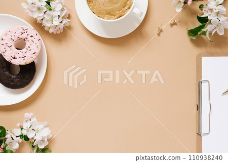 Blogger's flat lay. A cup of coffee, donuts, apple blossoms, a tablet on a beige background with a copy space 110938240