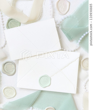 Card and envelope near light green and beige decorations and silk ribbons on white table top view, mockup 110938885