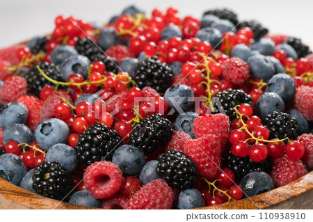 Fresh raspberries, blackberries, redcurrant and blueberries in a wooden bowl 110938910