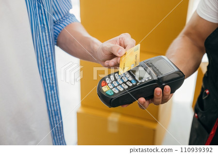 Family completes the move paying via credit card. Worker holds a box. Professional movers ensure efficient home relocation. Teamwork and service shown. Moving Day Concept 110939392