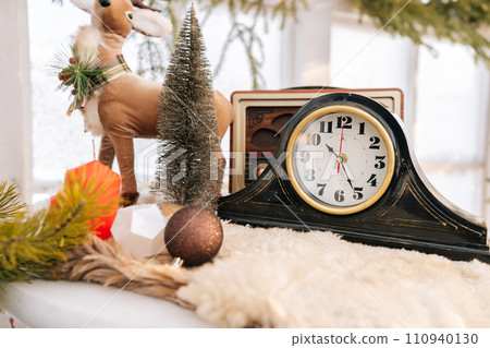 Bright composition of Christmas room interior with stylish wreath, clock, small xmas tree, ball on background of frozen window on sunny winter day. Christmas decorations, preparing for festive season. 110940130