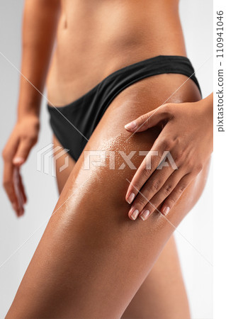 Woman applying care oil on her thigh Woman applying care oil on her thigh 110941046