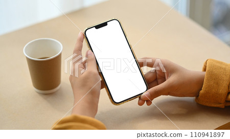 Closeup young woman holding mobile phone on working desk with paper cup of coffee Closeup young woman holding mobile phone on working desk with paper cup of coffee 110941897