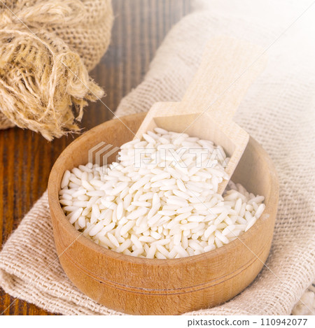 White uncooked Thailand jasmine rice in small burlap bag with wooden spoon on wood tablle on sunlight White uncooked Thailand jasmine rice in small burlap bag with wooden spoon on wood tablle on sunlight 110942077