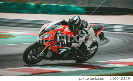 Racing motorbike rider in helmet and gear racing at high speed on race track with motion blur Racing motorbike rider in helmet and gear racing at high speed on race track with motion blur 110942369
