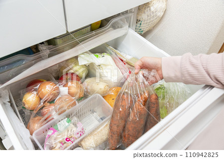 A woman takes out a bag of carrots from the vegetable drawer of the refrigerator. 110942825