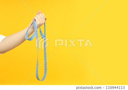Tape measuring body parameters, in a man's hand, on a yellow background. Tape measuring body parameters, in a man's hand, on a yellow background. 110944113