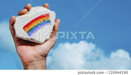 man holds a rock with a rainbow flag painted on it 110944190