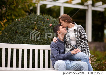 Autumn Romance: Young Couple Embracing and Kissing on Park Bench. Young couple kissing and rejoices at the lake. lovely young couple kissing outdoors in autumn. Embraced in Autumn's Warmth: Couple's Autumn Romance: Young Couple Embracing and Kissing on Park Bench. Young couple kissing and rejoices at the lake. lovely young couple kissing outdoors in autumn. Embraced in Autumn's Warmth: Couple's 110944535