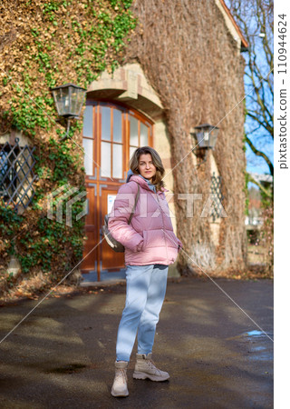 Young beautiful pretty tourist girl in warm hat and coat with backpack walking at cold autumn in Europe city enjoying her travel in Bietigheim-Bissingen, Deutschland. Outdoor portrait of young tourist 110944624
