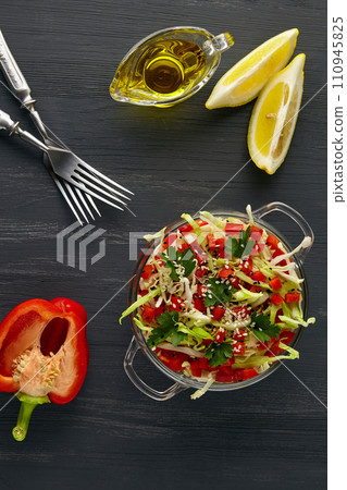 Colorful fresh vegetable salad in a glass bowl on a black wooden table. Vegetarian salad of cabbage, sweet pepper and parsley with sesame and cumin seeds and olive oil and lemon dressing Colorful fresh vegetable salad in a glass bowl on a black wooden table. Vegetarian salad of cabbage, sweet pepper and parsley with sesame and cumin seeds and olive oil and lemon dressing 110945825