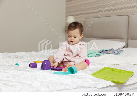 happy cute little child girl playing and pretending drinking tea from toy cups on bed 110946037
