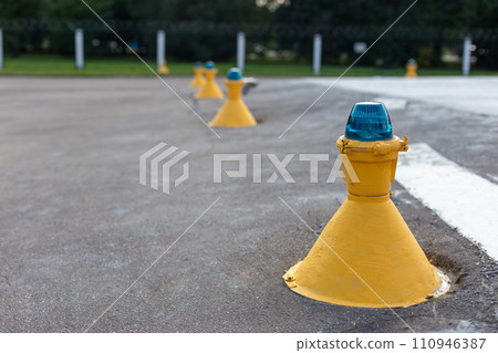Row of yellow airfield ground lights with blue tops, used for runway and taxiway guidance at an airport 110946387
