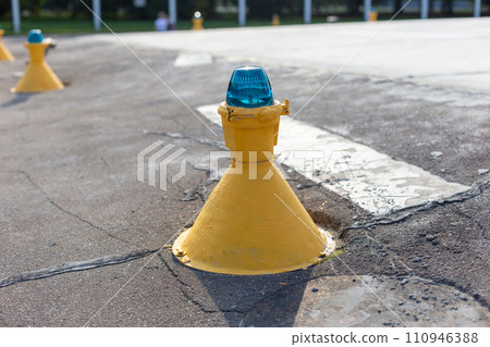 Close-up of a yellow runway marker with a blue light, indicating directions on the airport tarmac 110946388