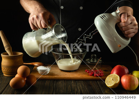 The chef prepares a milkshake with fruits in the kitchen using a hand-held electric mixer. The cook pours milk into a deep plate. Menu of delicious recipes for a hotel or restaurant The chef prepares a milkshake with fruits in the kitchen using a hand-held electric mixer. The cook pours milk into a deep plate. Menu of delicious recipes for a hotel or restaurant 110946449
