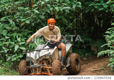 handsome asian man smiling while riding the atv through the difficult terrain handsome asian man smiling while riding the atv through the difficult terrain 110947038