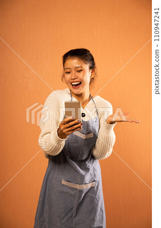 Happy Asian girl wearing apron using phone for video call 110947241