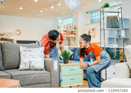 two shop assistants work together to move a small cabinet two shop assistants work together to move a small cabinet 110947260