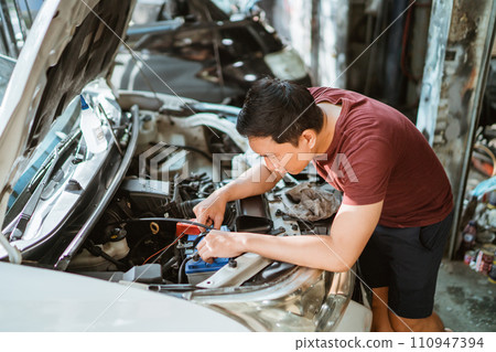 A male mechanic checks a car battery at a service station 110947394