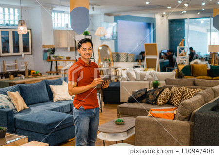 handsome male shop owner smiling using a tablet in furniture store 110947408