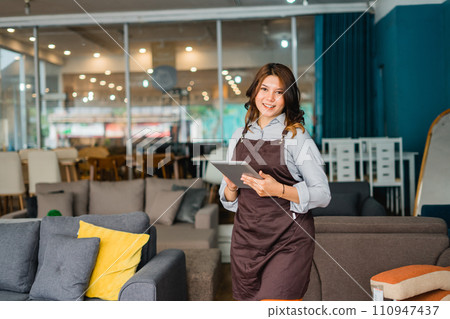 smiling female waitress in apron using a tablet digital in furniture store 110947437
