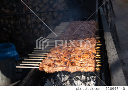A lot of juicy meat kebabs in a row on the grill. Meat pieces strung on wooden skewers on the grill. The process of cooking kebabs with a lot of smoke. Cooking in nature 110947440