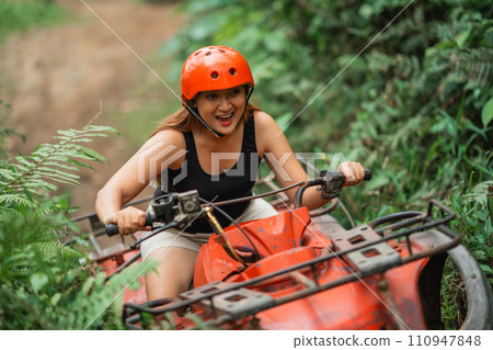 young asian woman smiling while riding the atv through the difficult terrain young asian woman smiling while riding the atv through the difficult terrain 110947848