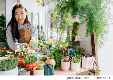 Small business, home decor concept. Professional young Asian female floral store owner arranges flower pots, takes stock daily routine of running a small business. Small business concept. 110948391
