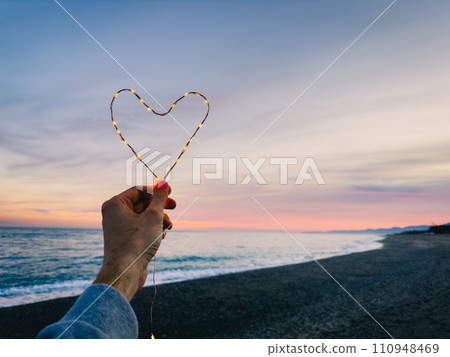 Holding a heart symbol made with bright fairy lights 110948469
