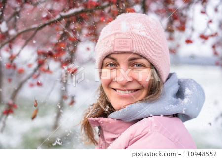 Winter Elegance: Portrait of a Beautiful Girl in a Snowy European Village. Winter lifestyle portrait of cheerful pretty girl. Smiling and having fun in the snow park. Snowflakes falling down 110948552