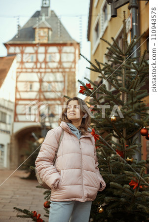A beautiful girl stands on the street of the old European town of Bietigheim-Bissingen in Germany on Christmas Eve. City streets are decorated with Christmas trees and New Year's decorations, tourism A beautiful girl stands on the street of the old European town of Bietigheim-Bissingen in Germany on Christmas Eve. City streets are decorated with Christmas trees and New Year's decorations, tourism 110948578