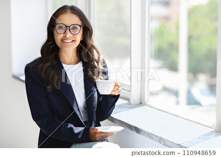 Mature businesswoman wearing eyeglasses drinking coffee at office 110948659