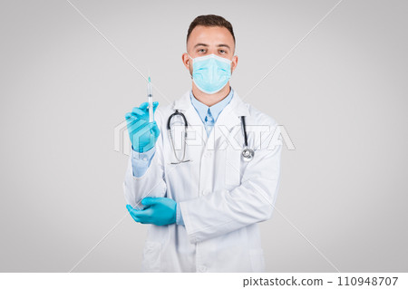 Doctor with mask and gloves holding a syringe, looking at camera 110948707