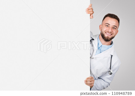 Cheerful male doctor peeking from behind a banner. 110948789