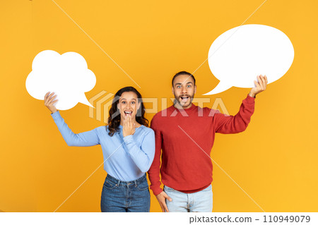 Shocked millennial couple holding empty speech bubbles on yellow 110949079