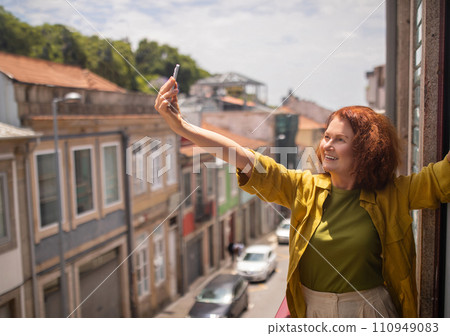 Joyful senior woman stretching out her arm and taking selfie on balcony 110949083