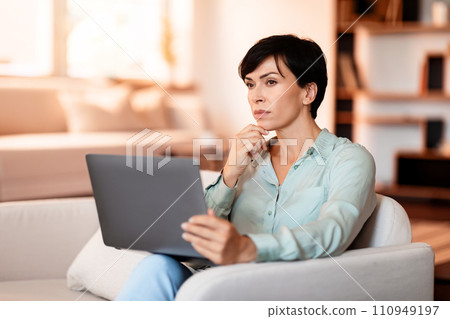 Thoughtful middle aged European woman with laptop in living room 110949197