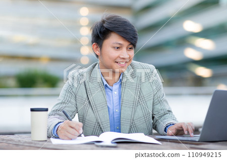 Korean entrepreneur man noting info near laptop against cityscape outside Korean entrepreneur man noting info near laptop against cityscape outside 110949215