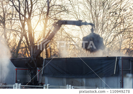 Modern truck crane arm loading trailer heap dung manure straw fertilizer from horse cow farm yard countryside warm sunset background. Steaming smoking warm dunghill bio organic compost byproduct 110949278