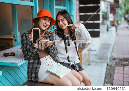 two girls show the screen with a hand gesture of offering something 110949281