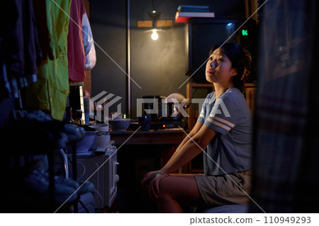 Girl sitting on bed in small apartment Girl sitting on bed in small apartment 110949293