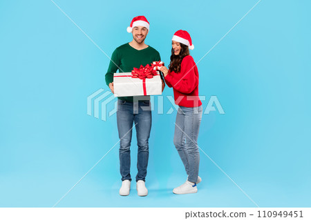 Young couple with Santa hats holding wrapped gift boxes, studio 110949451