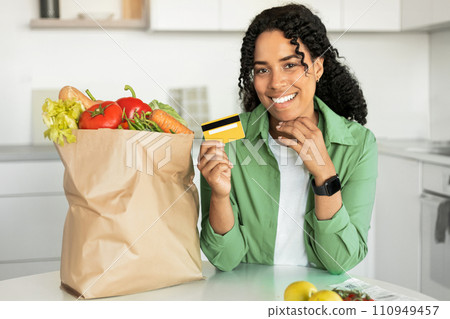 Black woman showcases credit card for grocery shopping in kitchen Black woman showcases credit card for grocery shopping in kitchen 110949457