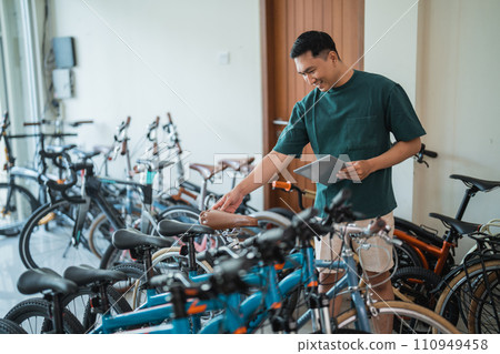 young man checks the saddle of bicycle while using a tablet young man checks the saddle of bicycle while using a tablet 110949458