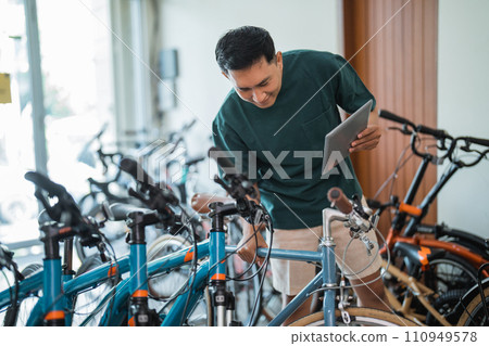 young man looking at a new bicycle frame while using a tablet 110949578